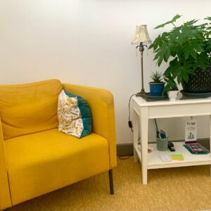 A room with a yellow chair and a plant on a stand